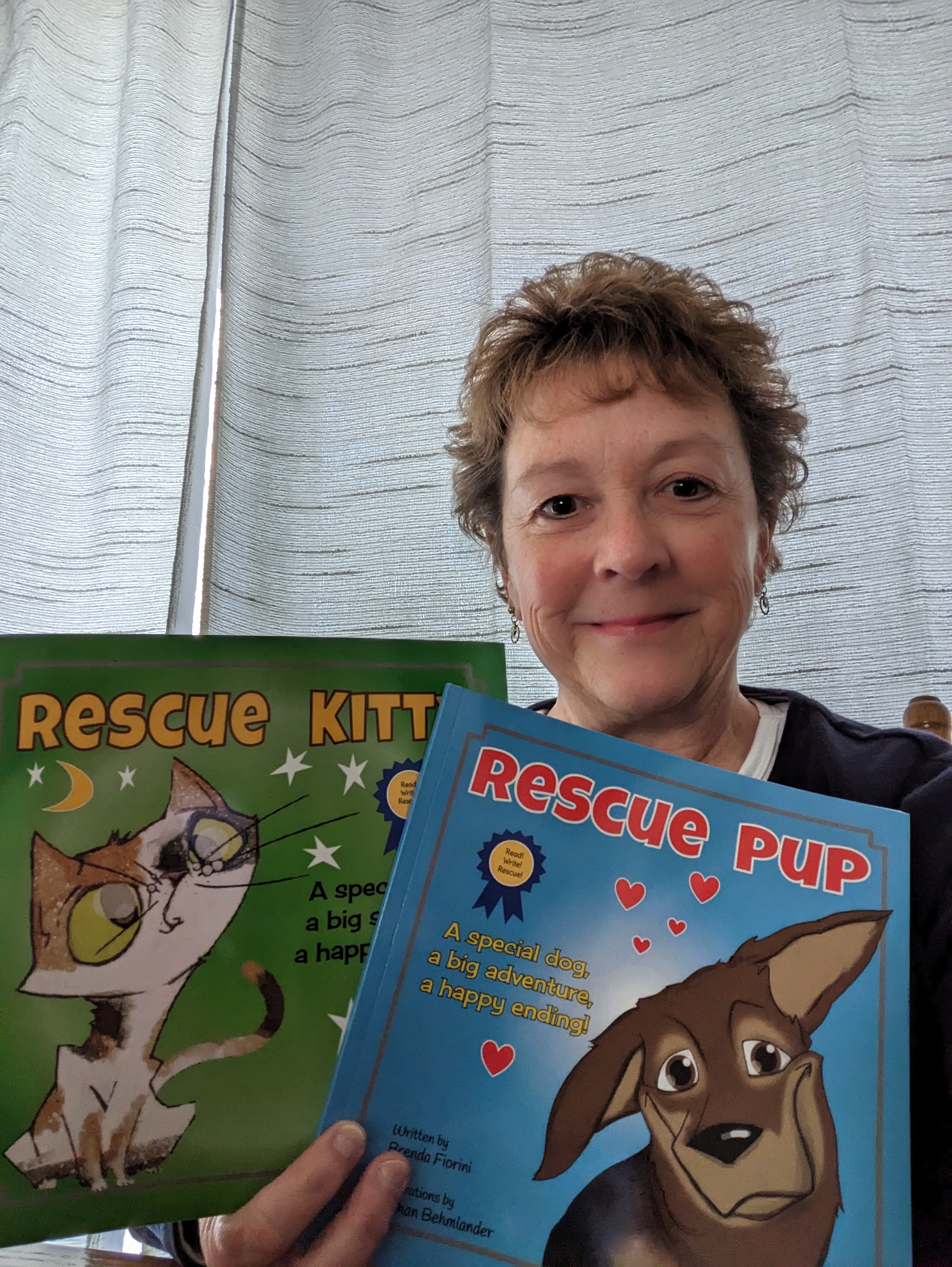 Photo of Brenda Fiorini smiling and holding copies of two books she has written: Rescue Kitty and Rescue Pup